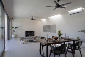 A modern living room with a sofa, TV, and dining area with chairs and a table set for a meal. - Vega 2BR Luxury Private Pool Villa - Ungasan (South Kuta)