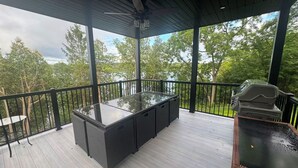 Une terrasse extérieure dotée d’une table et de chaises à plateau en verre, entourée d’une rambarde, et offrant une vue sur une zone boisée.