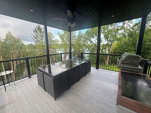 An outdoor deck with a glass-top table and chairs, surrounded by a railing, overlooking a wooded area. - Newly Built Luxury 7BR Big Rideau Lake Cottage | Sleeps 20 (Rideau Lakes)