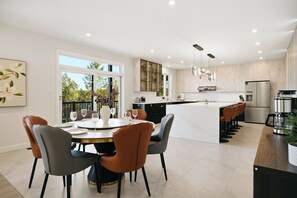 Une cuisine moderne dotée d’un îlot central, d’un coin repas avec des chaises et offrant une vue sur l’extérieur.