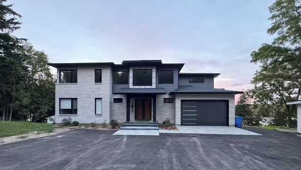 Une maison moderne à deux étages, dotée d’un garage, d’une allée et d’un petit jardin devant.