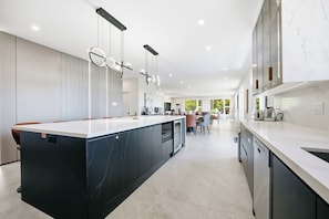 Une cuisine moderne dotée d’un îlot central, d’appareils électroménagers intégrés et de luminaires suspendus.