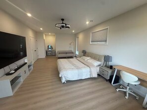 A modern bedroom with a bed, desk, chair, TV, and a ceiling light. - Newly Built Luxury 7BR Big Rideau Lake Cottage | Sleeps 20 (Rideau Lakes)