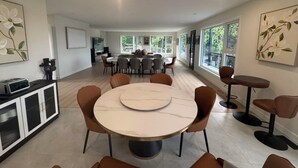 Un espace repas moderne avec une table ronde et des chaises, un coin cuisine doté d’un four encastré et de grandes fenêtres laissant entrer la lumière naturelle.