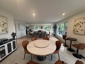A modern dining area with a round table and chairs, a kitchen area with a built-in oven, and large windows providing natural light. - Newly Built Luxury 7BR Big Rideau Lake Cottage | Sleeps 20 (Rideau Lakes)