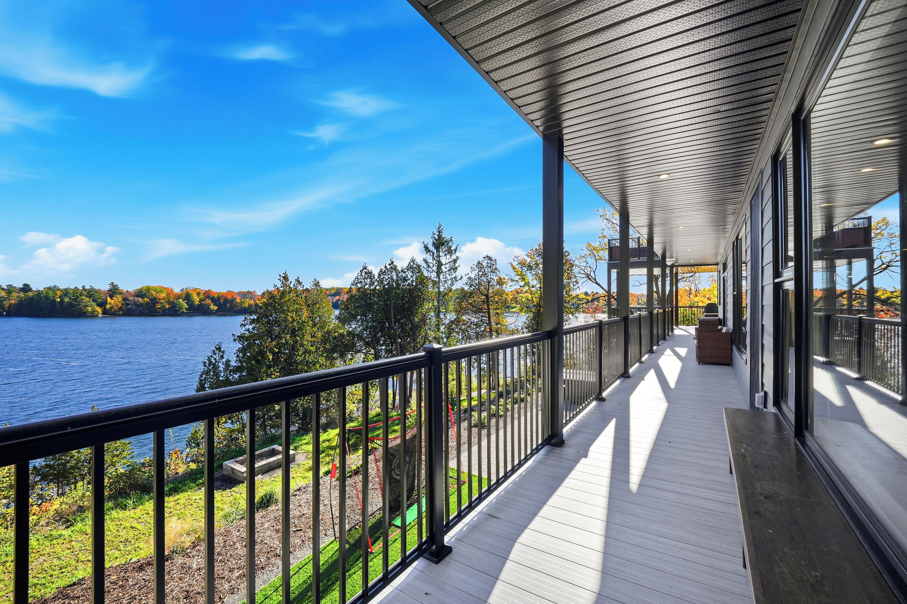 A covered outdoor deck with a view of a lake and autumn foliage.