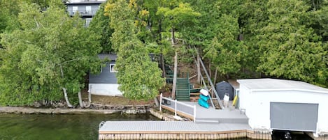 A dock extending into a body of water with a house in the background surrounded by trees.