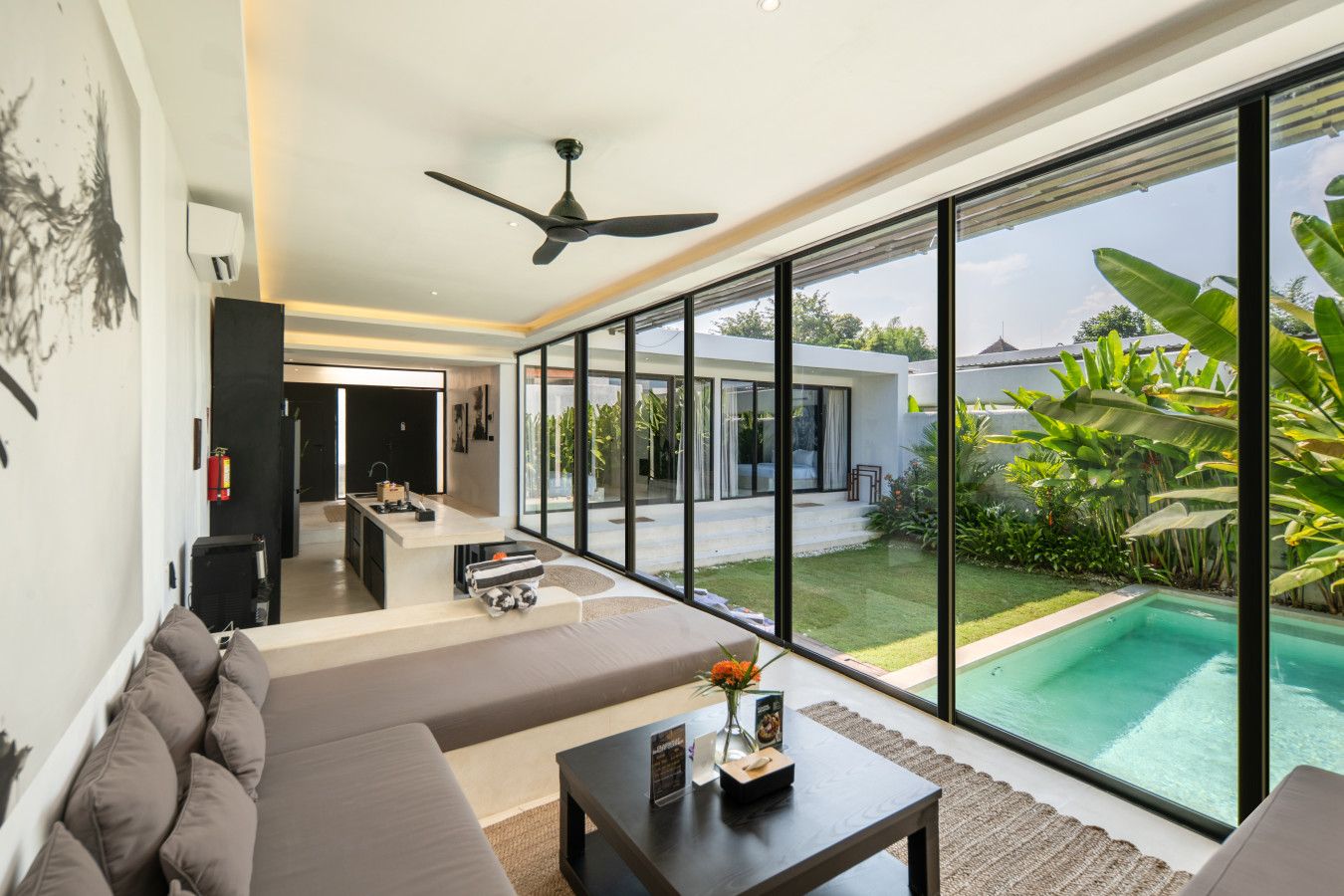 A modern living room with a large window, a ceiling fan, and a view of a swimming pool and garden.
