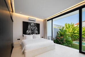 A modern bedroom with a large bed, a wall-mounted air conditioner, and a view of a lush garden. - Marea 2BR Luxury Private Pool Villa - Uluwatu (South Kuta)