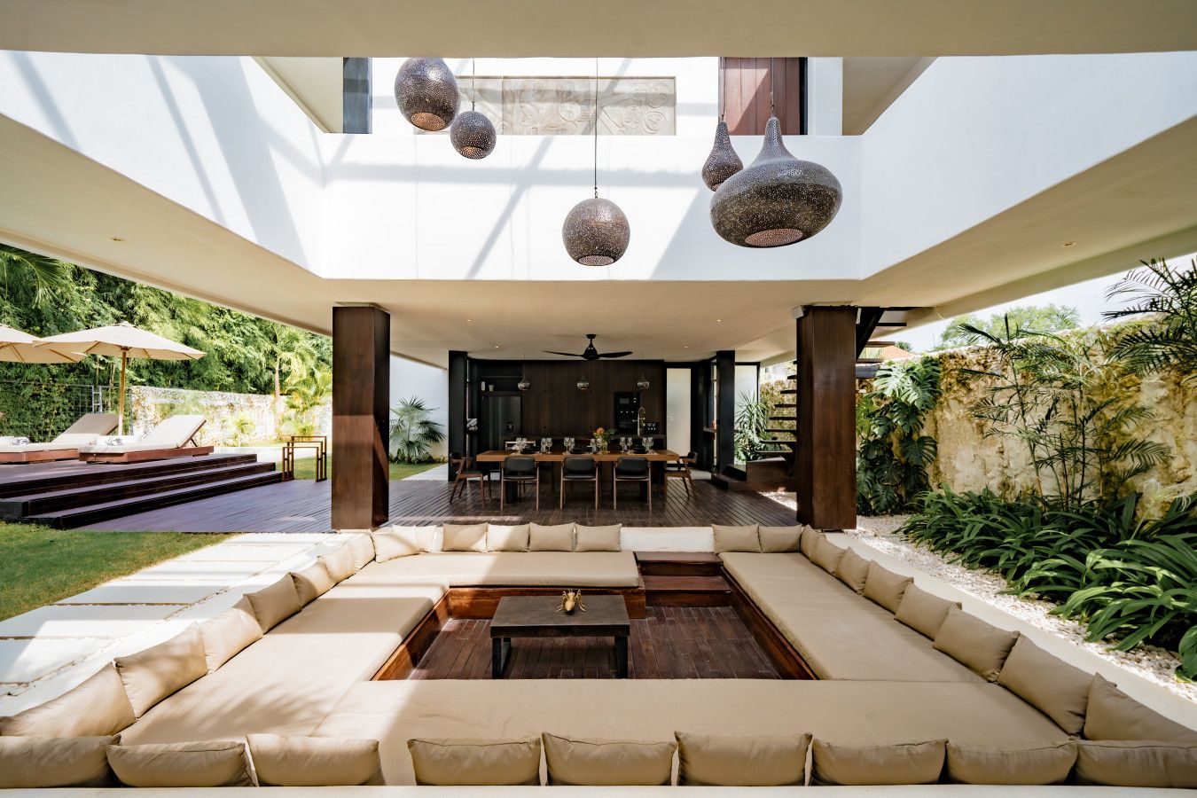 A modern outdoor living area with a dining table and chairs, surrounded by cushioned seating and a fire pit.