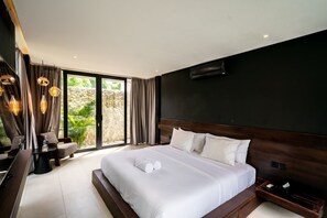 A modern bedroom with a large bed, a desk, and a view of greenery through the window. - Brezza 3BR Luxury Private Pool Villa - Uluwatu (South Kuta)