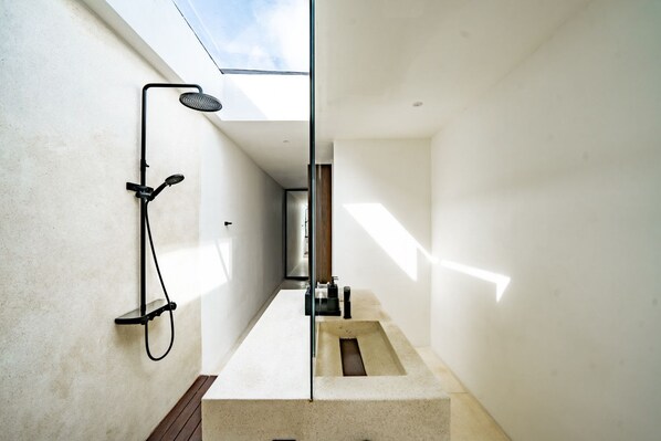 Ein modernes, minimalistisches Badezimmer mit einem Oberlicht, einer Dusche und einem großen Spiegel.