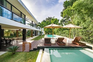 Ein modernes Haus mit Schwimmbad, Sitzgelegenheit im Freien und üppigem Grün.