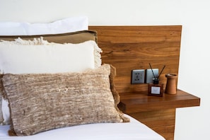 Ein Bett mit weißen und braunen Kissen, ein Holz-Kopfbrett und ein Nachttisch mit einer Holzlampe, einem Telefon und einer Kerze.