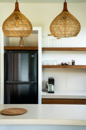 A kitchen with a black refrigerator, a coffee maker, and wicker pendant lights. - Majo 1BR Romantic Villa, 3 Min to Thomas Beach (South Kuta)
