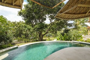 A swimming pool with a curved edge, surrounded by lush greenery and trees. - Ahura 5BR Oceanview in Bingin Uluwatu (Kecamatan Kuta Selatan)