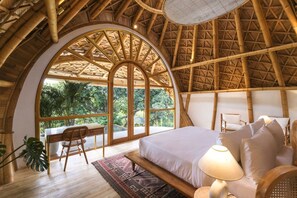 A room with a large arched window, a bed with pillows, a bedside table, a chair, and a lamp. - Ahura 5BR Oceanview in Bingin Uluwatu (Kecamatan Kuta Selatan)
