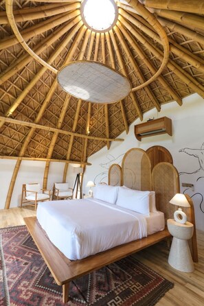 A room with a bed, two chairs, a round table, and a wall-mounted air conditioning unit. - Ahura 5BR Oceanview in Bingin Uluwatu (Kecamatan Kuta Selatan)