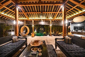 Ein geräumiger Innenbereich mit hoher Decke, Holzbalken und einer zentralen Sitzecke mit Sofas und einem Hängesessel.