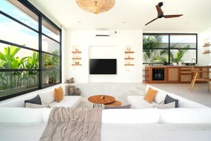 A modern living room with a large window, a flat-screen TV, a sofa, a coffee table, and a ceiling fan. - Villa Sofra 2BR Private Pool, 350mbps WiFi- Bingin (South Kuta)