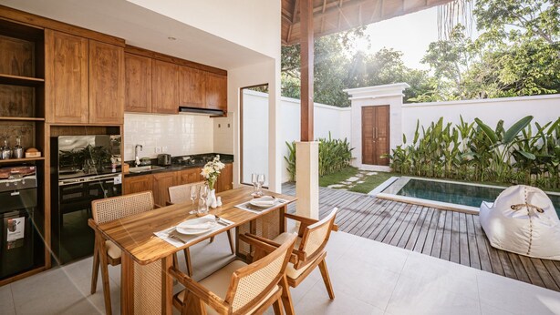 A modern kitchen with wooden cabinets, a dining area with a table and chairs, and a pool area with a wooden deck. - Parisula 1BR Villa with Pool in Bingin Uluwatu (South Kuta)