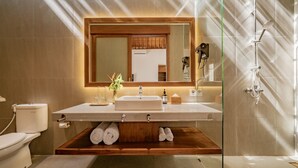 A modern bathroom with a large mirror, a sink, and a shower. There is a wooden shelf under the sink holding towels. - Parisula 1BR Villa with Pool in Bingin Uluwatu (South Kuta)