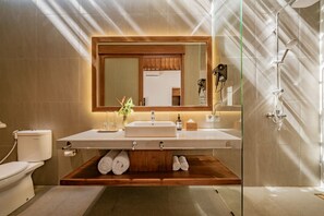 A modern bathroom with a large mirror, a sink, and a shower. There is a wooden shelf under the sink holding towels. - Parisula 1BR Villa with Pool in Bingin Uluwatu (South Kuta)