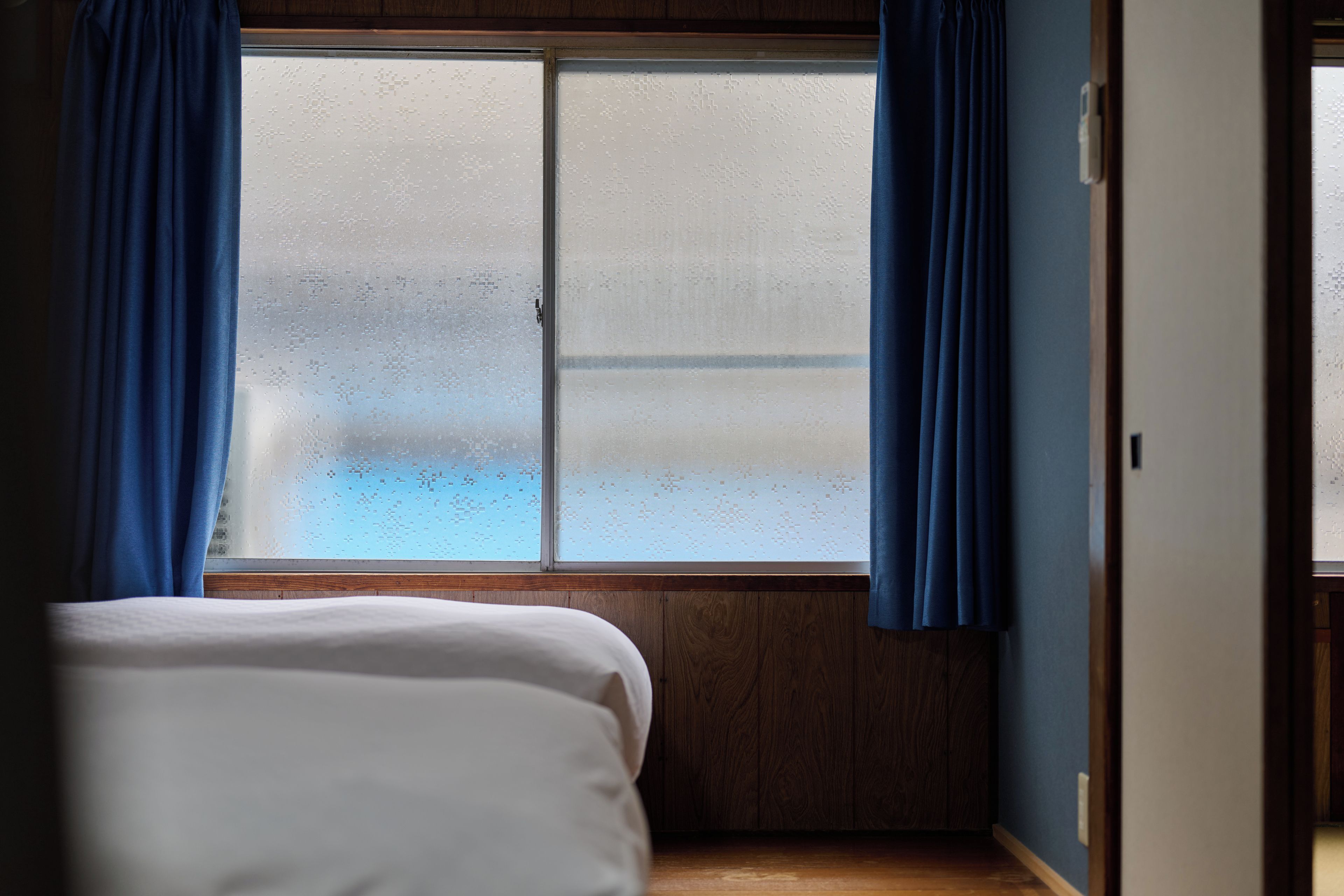 A room with a bed, a window with frosted glass, and blue curtains.