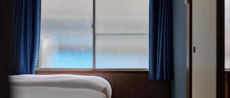 A room with a bed, a window with frosted glass, and blue curtains.