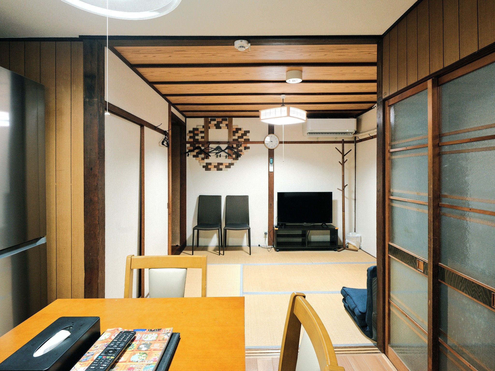 Quarto japonês tradicional com tatames, uma televisão e uma mesa de jantar com cadeiras.