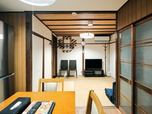 Ein traditioneller japanischer Raum mit Tatami-Böden, einem Fernseher und einem Esstisch mit Stühlen.