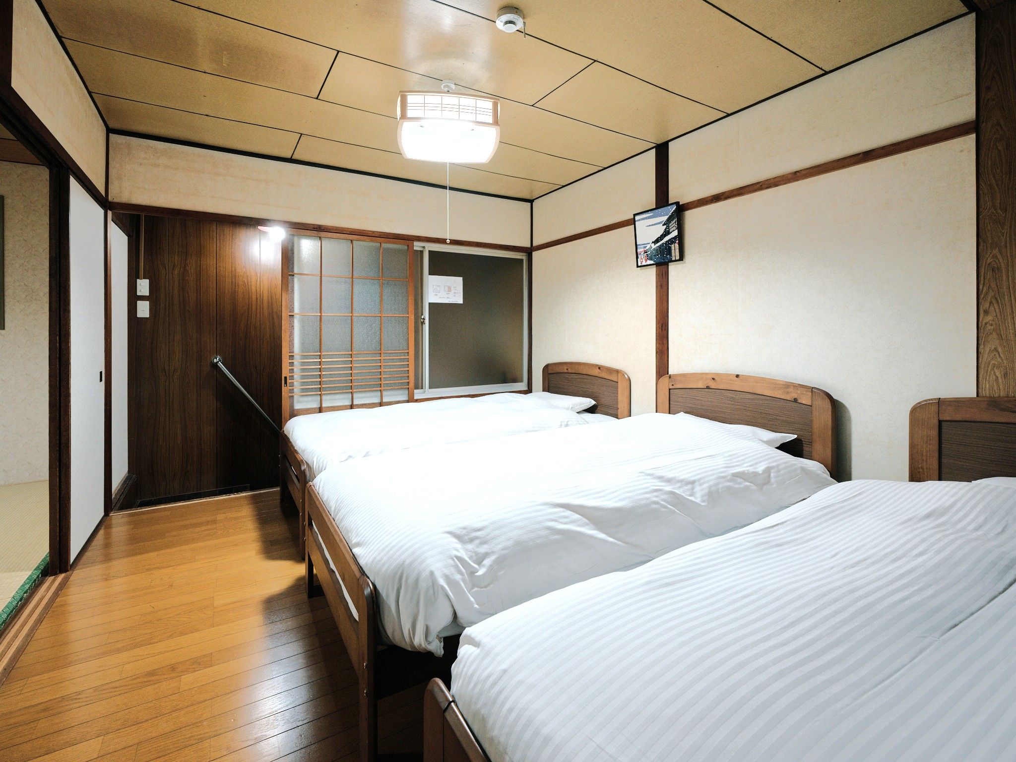 Une chambre d’hôtel avec deux lits, un plancher en bois, une porte coulissante et un luminaire au plafond.