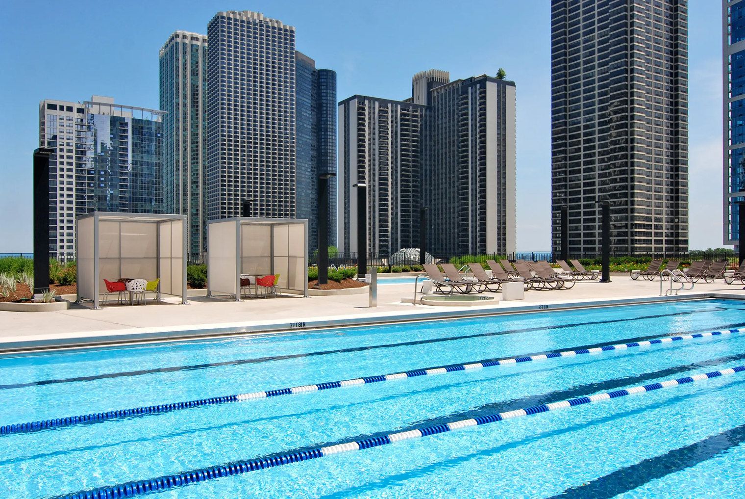 Una piscina con corsie divisorie, poltrone a sdraio e sullo sfondo edifici alti.