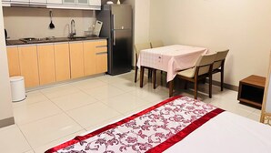 A compact kitchen with a refrigerator, sink, and cabinets, a dining table with chairs, and a bed with a floral bedspread. - One Uptown Residence BGC Modern BGC Home | 300Mbps + Workspace (Makati City)