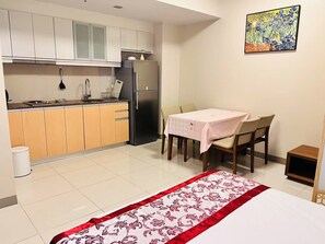 Eine kompakte Küche mit Kühlschrank, Spüle und Schränken, ein Esstisch mit Stühlen und ein Bett mit floralem Überwurf.