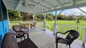 A covered outdoor area with wicker furniture, a patterned floor, and a view of a grassy landscape. - Private Gated Tropical Cottage Near Hilo & Pāhoa –Peaceful, Secure Island Escape (Keaau)