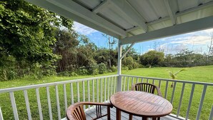 A covered outdoor seating area with a table and chairs, surrounded by a white railing, overlooking a grassy landscape. - Private Gated Tropical Cottage Near Hilo & Pāhoa –Peaceful, Secure Island Escape (Keaau)