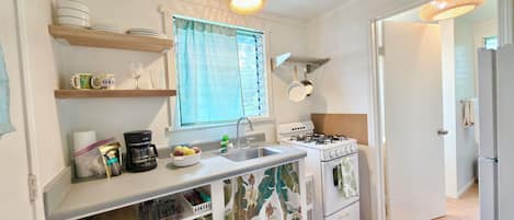 Una cocina compacta con estufa a gas, un lavamanos y un ventanal con cortinas.