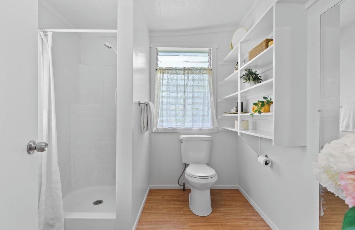 A compact bathroom with a shower, toilet, and a window with a curtain.