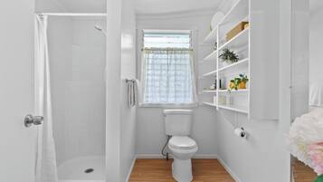 A compact bathroom with a shower, toilet, and a window with a curtain.