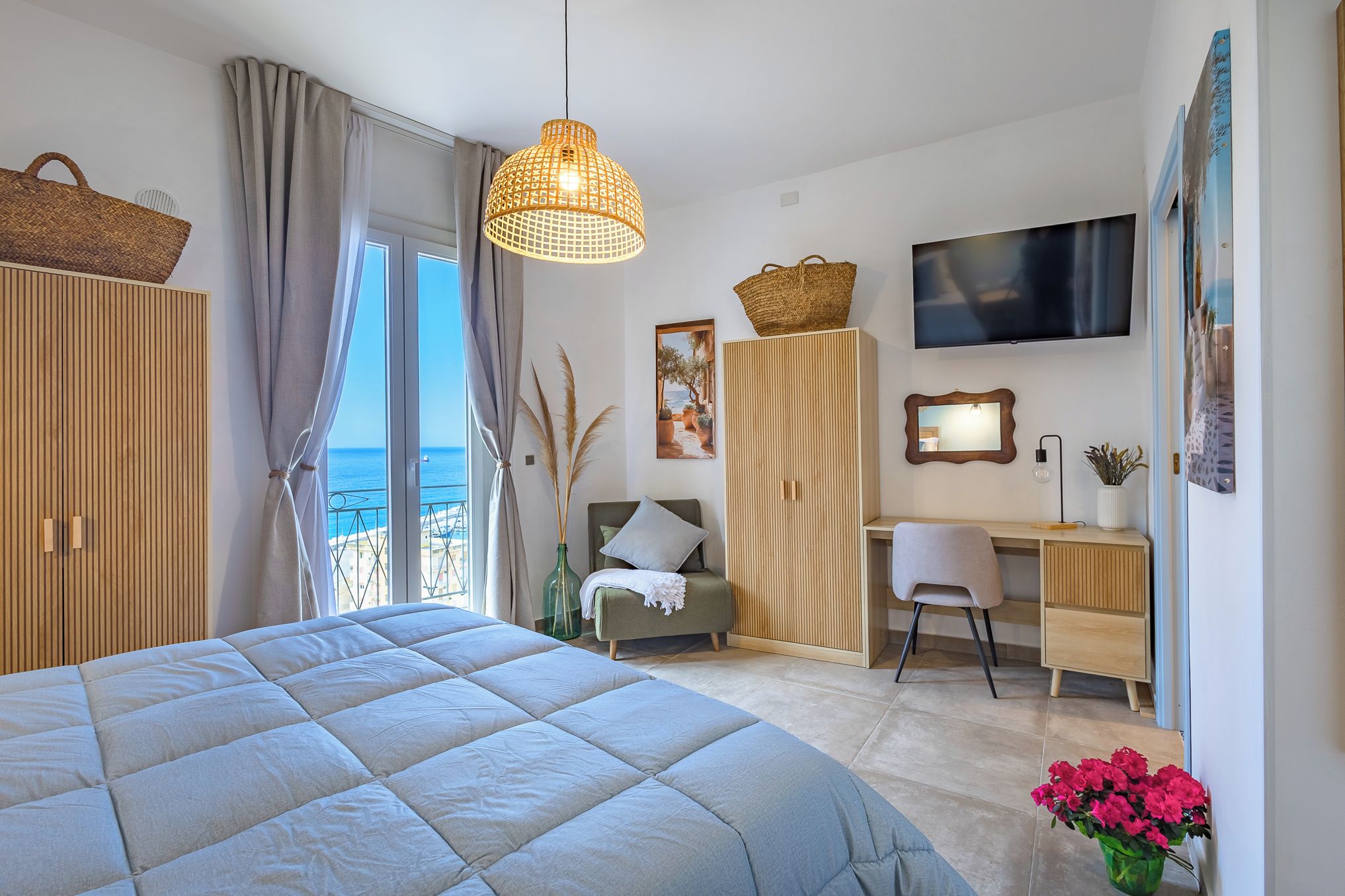 Une chambre avec un grand lit, un bureau, une chaise, une télévision et une vue sur la mer.