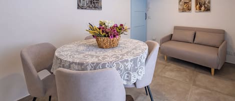 A dining area with a round table, chairs, and a floral centerpiece. There is a sofa and artwork on the walls.