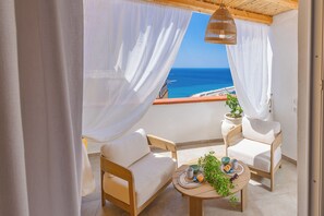 A balcony with two white cushioned chairs, a small table with a plant, and a view of the sea. - New & Panoramic Harbor Views - Sanciolu House (Sciacca)