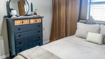 Une chambre à coucher avec un lit, une commode à tiroirs, un miroir et une fenêtre avec des rideaux.