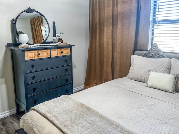 A bedroom with a bed, a dresser with drawers, a mirror, and a window with curtains.