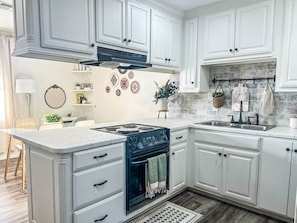 A kitchen with white cabinetry, a black stove, and a stone backsplash.