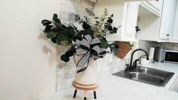 Une cuisine avec un plan de travail blanc, un évier en acier inoxydable et une plante décorative ornée d’un ruban noir et blanc.
