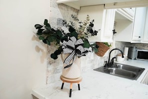 A kitchen with a white countertop, a stainless steel sink, and a decorative plant with a black and white bow.