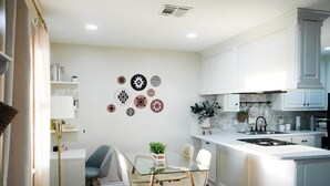 Cozinha moderna com armários brancos, mesa de jantar de vidro e obras de arte decorativas nas paredes.