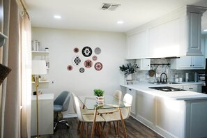 A modern kitchen with white cabinets, a glass dining table, and decorative wall art. - ModWest Escape | Pets Welcome | Near I-40 & Rt 66 (Weatherford)